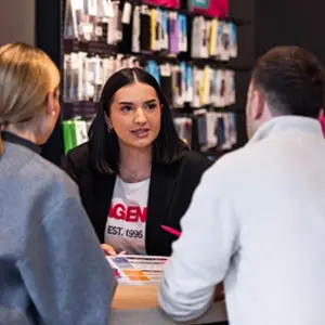 Eine Beraterin erklärt zwei Kunden im Mobilfunkshop Tarife und Smartphone-Angebote.