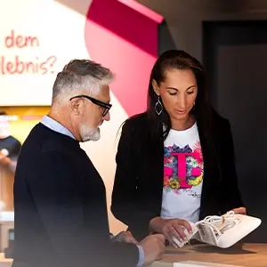 Eine Mitarbeiterin berät einen Kunden im Telekom-Shop zu einem weißen Smartphone.