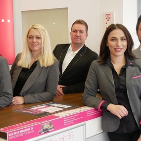 Fünf Telekom-Mitarbeiter stehen freundlich im modernen Telekom-Shop mit Beratungstheke.