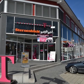 Modernes Telekom-Geschäft mit großer Glasfassade und Sternenbäck-Filiale im Erdgeschoss.