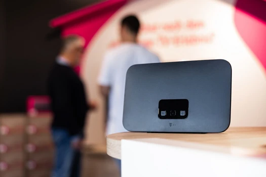 WLAN-Router auf Tresen in Telekom-Shop, zwei Personen im Hintergrund im Beratungsgespräch.