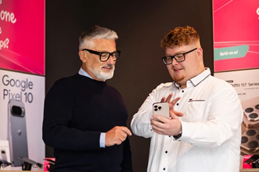 Zwei Männer in einem Handyshop betrachten gemeinsam ein Smartphone am Verkaufstresen.