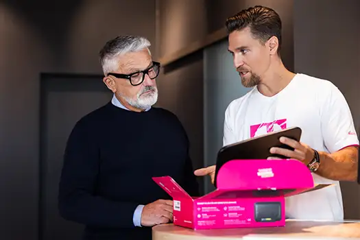 Mann erklärt Senior ein Tablet und Magenta-Router im Telekom-Shop.