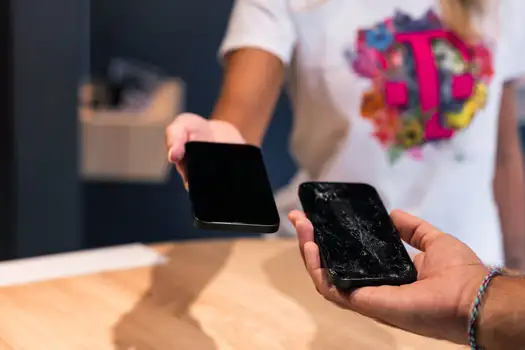 Eine Person tauscht ein kaputtes Smartphone gegen ein neues Handy im Telekom-Shop aus.